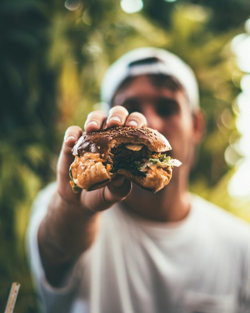 A man holds a juicy cheeseburger outdoors in daylight, highlighting its deliciousness and freshness.
