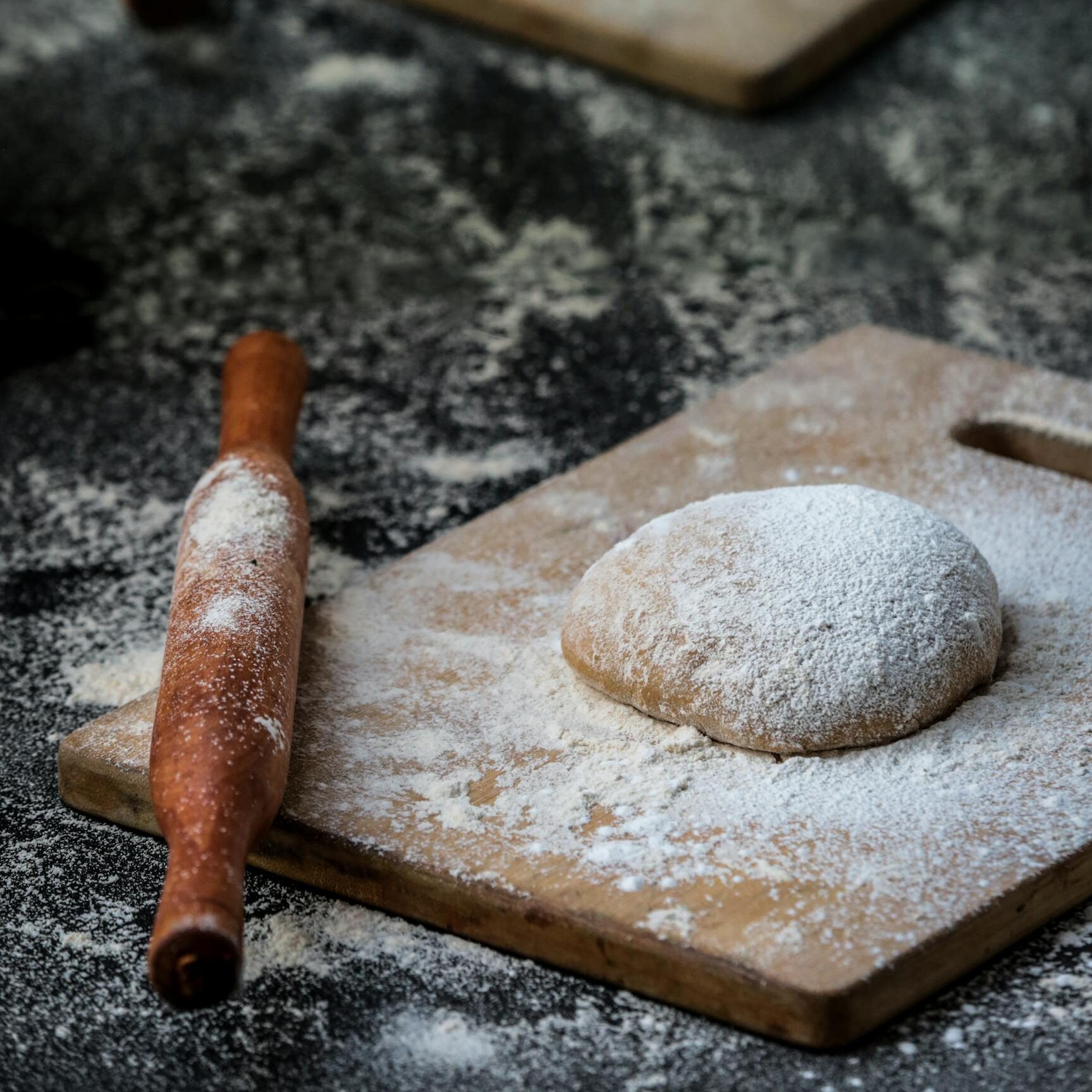 Fresh pizza dough on wooden boards with a dusting of flour and rolling pins.