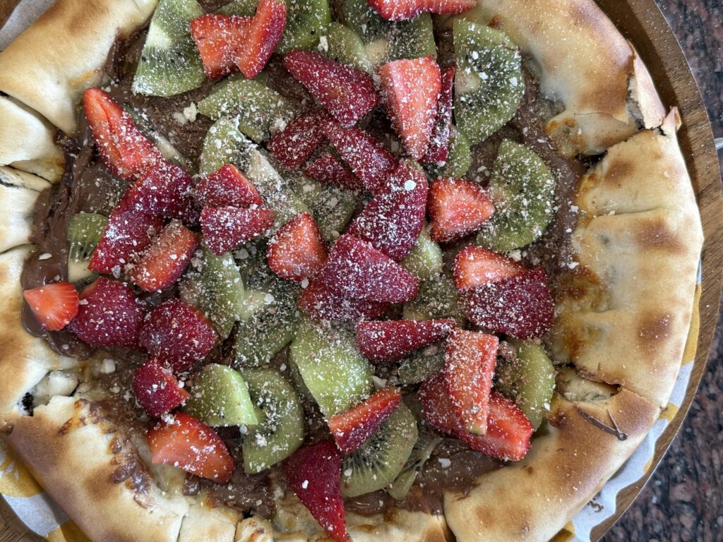 Scrumptious dessert pizza topped with fresh strawberries and kiwi slices.