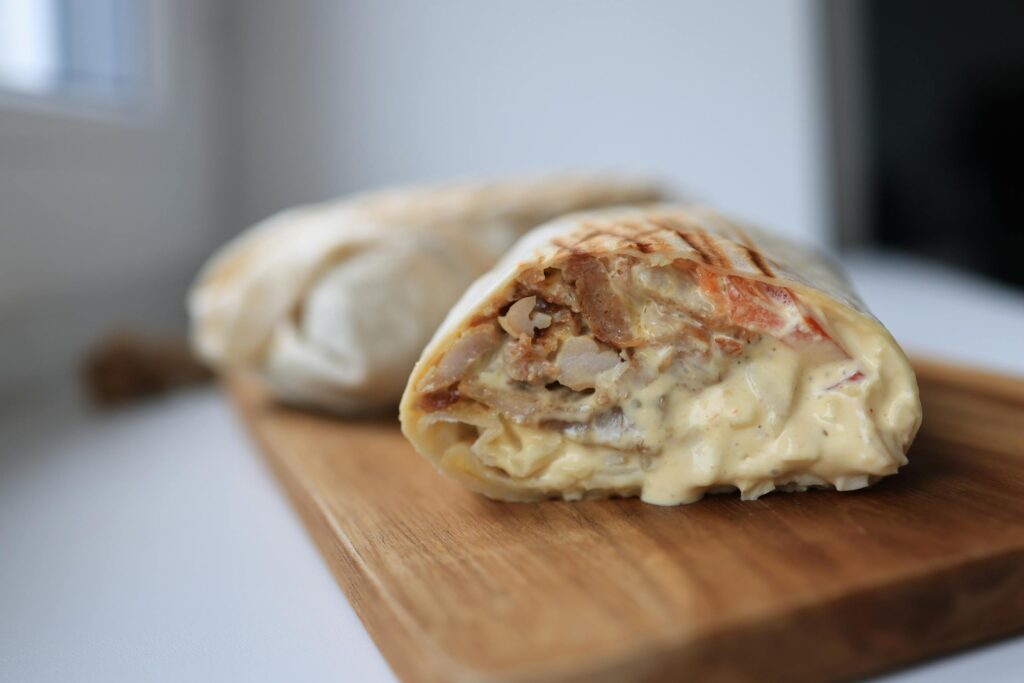 Tasty chicken wrap filled with creamy sauce on a wooden cutting board.