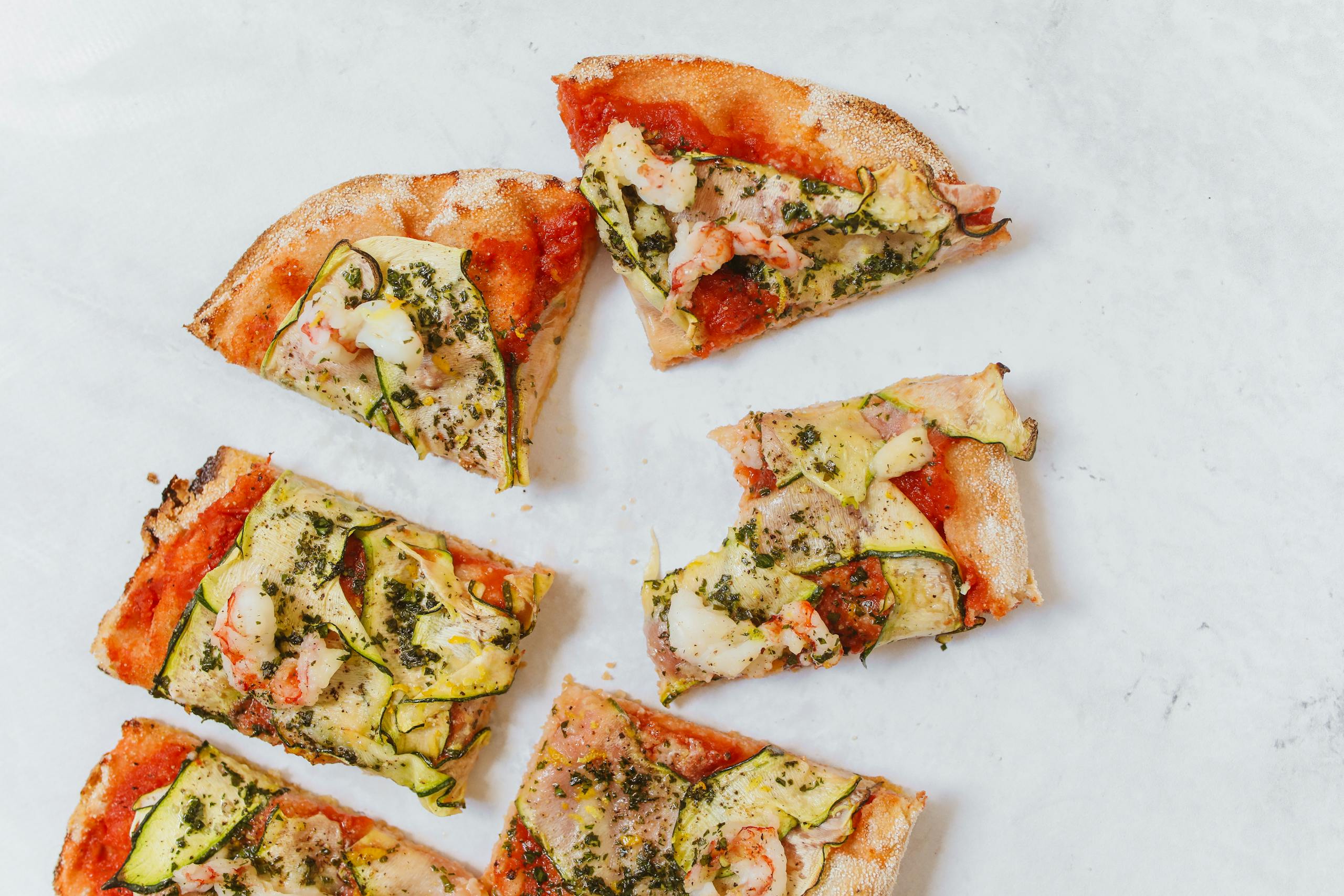 Top view of sliced Italian pinsa with zucchini and herbs, perfect for food lovers.